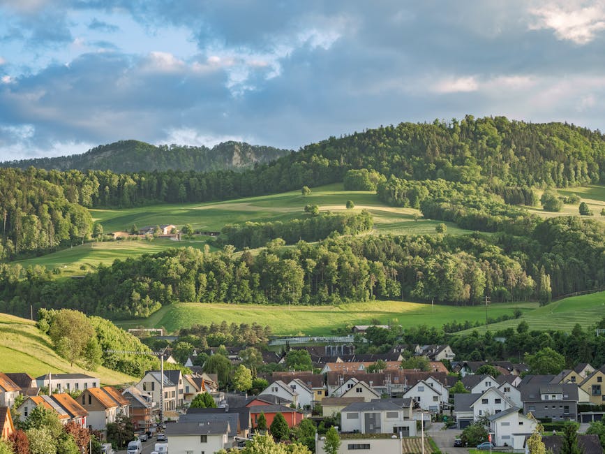 A panoramic view of a residential area with a mixture of multi-storey and terraced houses in Mill Hill, set against a backdrop of rolling green hills under a partly cloudy sky, as seen from an elevate